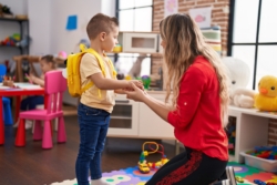 Teacher and toddler wearing backpack standing at kindergarten