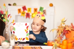 Boy in paper turkey hat writing I am thankful for.